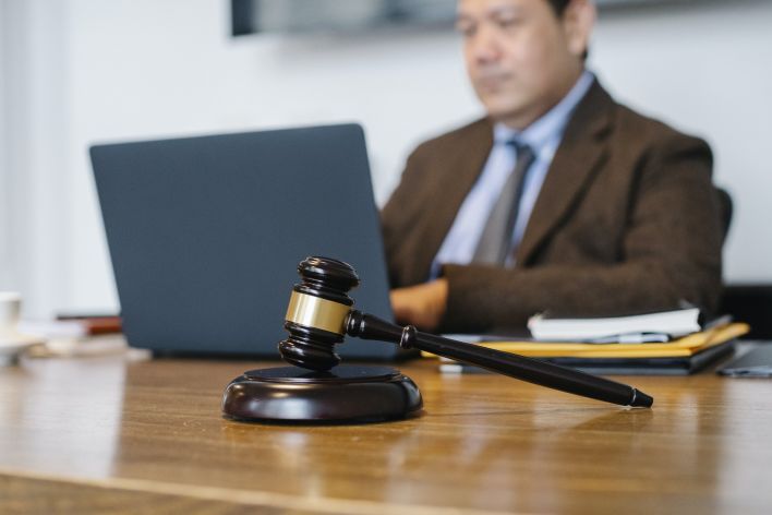 Crop concentrated Asian male judge in formal clothes sitting using modern netbook while working in law office